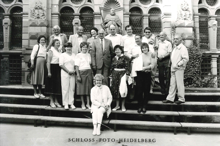 Mehrerer Menschen auf einem Gruppenbild bei einem Ausflug nach heidelberg, im Hintergrund eine historische Fassade des Heidelberger Schlosses