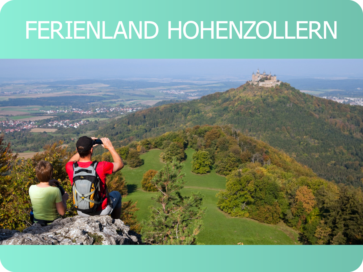 Zwei Wanderer blicken mit einem Fernglas von einem Aussichtspunkt auf die Burg Hohenzollern